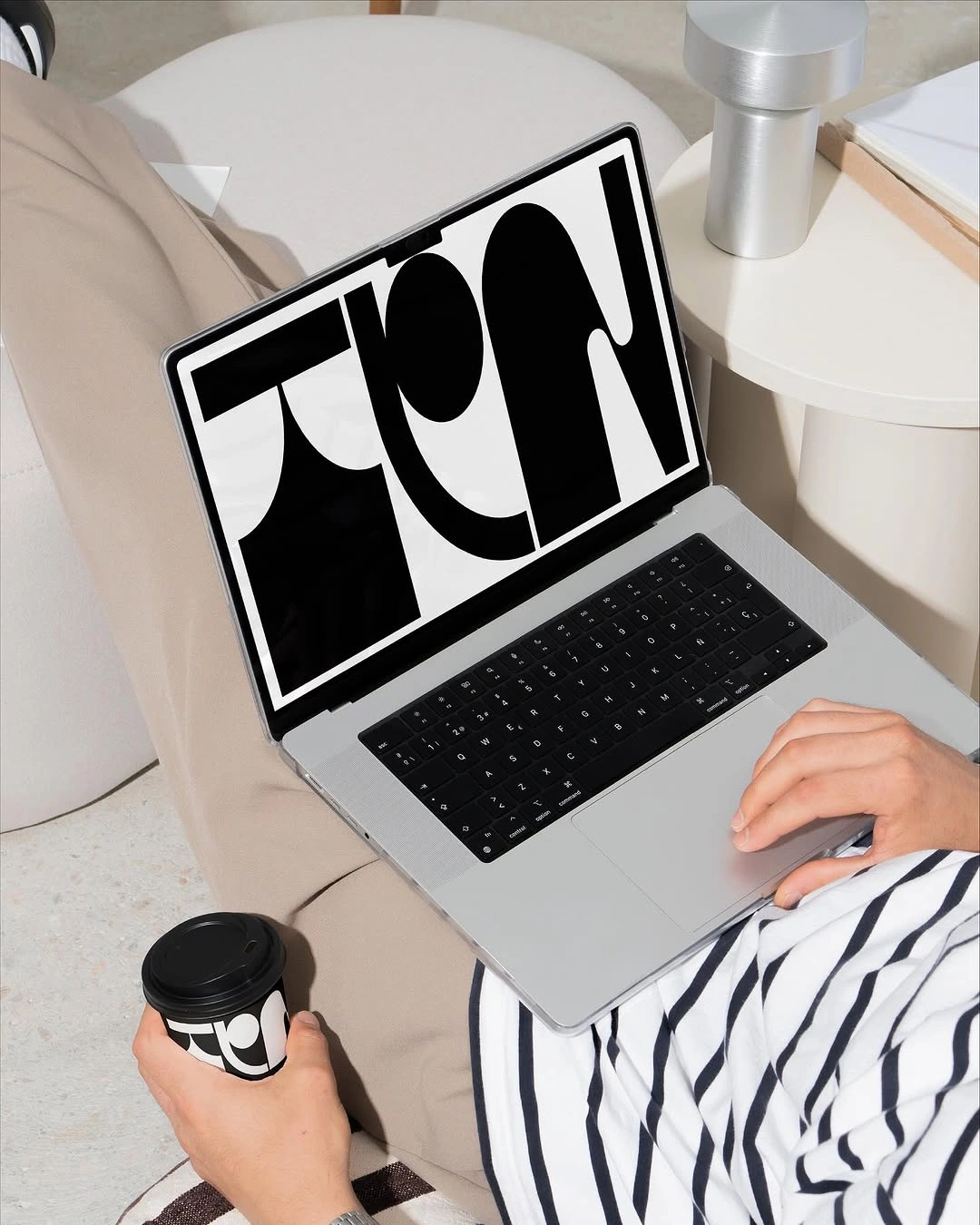 A laptop on a lap showing a bold black-and-white typographic identity